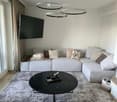 Modern living room with a grey sectional sofa, decorative pillows, a black coffee table, a large television mounted on the wall, and a grey shag rug.