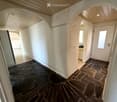 A narrow hallway with white walls, stone flooring, and arched doorways leading to other rooms. The ceiling is light-colored with recessed lighting.