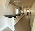 Modern kitchen with white cabinets, black countertop, stainless steel sink, and built-in oven. Light-colored tiled floor and wooden ceiling.