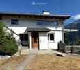 Two-story white house with a wooden front door, large windows, and a balcony overlooking a mountainous landscape.