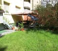 Garden with green grass, potted plants, a swing chair, a table with chairs, and an umbrella providing shade.