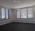 Empty room with white walls, dark tiled floor, and large windows with blinds.