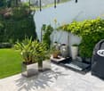 Well-maintained garden with a variety of potted plants, a neatly trimmed lawn, and a covered barbecue area.