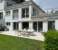 Modern house with a spacious outdoor patio area featuring a dining set, surrounded by greenery and featuring a balcony on the upper level.