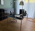Modern office space with a wooden floor, a black desk, a black office chair, a laptop, a screen, a keyboard, a mouse, a floor lamp, a black cabinet, and framed pictures on the wall.