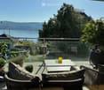 Balcony with a view of the water and mountains, featuring a table, chairs, and potted plants.
