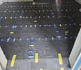Empty room with a dark grey floor, marked with blue and yellow spacers for tile installation. No furniture or equipment present.