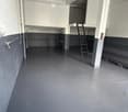 Empty room with grey walls, dark grey floor, and a ladder leading to an upper level. No furniture or equipment visible.