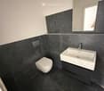 Modern bathroom with black marble tiles, white toilet, white sink, and a mirror above the sink.
