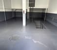 Empty industrial-style room with a concrete floor, metal pillars, and a ladder leading to an upper level. No furniture or equipment is present.