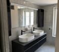 Modern bathroom with two white sinks, sleek black faucets, a large mirror, and dark cabinets.