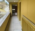 Balcony with yellow walls, white tiled floor, metal railings, and a view of a hillside.