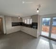 Modern kitchen, white cabinets, granite countertops, stainless steel appliances, grey tiled floor, sliding glass doors to balcony, overhead lighting