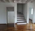 Empty hallway with wooden flooring, white walls, and a staircase leading upwards.