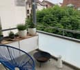Balcony with a blue wire chair, a black fire bowl, potted plants on a small cabinet, and a white pitcher.