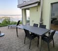 Balcony with a view, tiled floor, table with chairs, lounge chair, and potted plant.