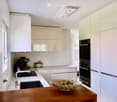 Modern kitchen with white cabinets, stainless steel appliances, a wooden table, and a bowl of fruit on the counter.