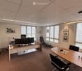 Office space with a desk, chairs, screens, a round table, and artwork on the walls.