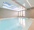 Indoor swimming pool area with a large skylight, modern tile walls, and a small waterfall feature.
