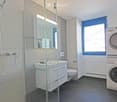 Modern bathroom with a glass-enclosed shower, a white sink with a mirror, a toilet, and a stacked washing machine and dryer.
