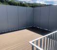 Wooden deck with white railing and surrounding white panels, overlooking a green, hilly landscape.