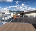 Wooden deck with metal railing, overlooking an industrial area with buildings and a distant mountain range under a partly cloudy sky.