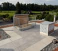 Roof terrace with concrete tiles, metal gate, and storage containers, surrounded by greenery and distant houses.