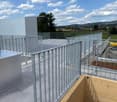 Modern rooftop terrace with metal railings, tiled floor, and scenic countryside view.