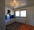 Modern kitchen with white cabinets, dark countertop, and wooden flooring. Features a stove, radiator, and large windows with blinds.