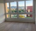 Empty room with wooden flooring and large windows offering a view of the city and surrounding landscape.