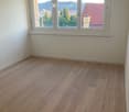 Empty room with light wooden flooring and large windows offering a view of the city and surrounding landscape.