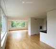 Empty room with light wooden flooring, white walls, large windows, and built-in white cabinetry.