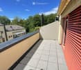Balcony with tiled floor, metal railing, and red shutters on adjacent building.