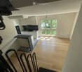 Modern kitchen with white cabinets, black countertop, and large windows letting in natural light. The floor is light wooden, and the space is clean and organized.