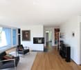 Modern living room with large windows offering a view, featuring a fireplace, sofa, armchairs, coffee table, TV, and floor lamp.