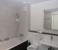 White tiled walls, bathtub, toilet, sink, mirror, power outlets, shelves