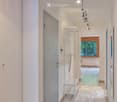 Modern hallway with wooden flooring, white walls, and a coat rack. Features recessed lighting and a large window at the end.