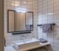 Modern bathroom with white tiles, a large sink, a mirror with built-in lighting, and a washing machine underneath the sink.