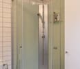Modern bathroom with a glass-enclosed shower, a toilet, and a towel hanging on a rack. The shower features a handheld sprayer and a built-in shelf holding toiletries.