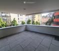 Empty balcony with tiled floor, white railing, and a view of surrounding buildings and greenery.