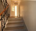 A narrow hallway with a staircase leading upwards, featuring a wooden handrail and a white door at the end.
