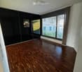 Empty room with wooden flooring, large windows with blinds, and a mirrored wardrobe unit on one wall.