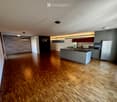 Modern kitchen with grey cabinets, a central island, and wooden flooring.