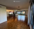 Open-plan space with wooden flooring, modern kitchen area with cabinets and appliances, large windows with sliding doors leading to a balcony, and recessed lighting.