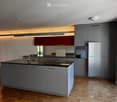 Modern kitchen with grey cabinets, a central island, stainless steel appliances, and wooden flooring.