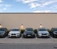 Five cars parked in a private parking area next to a building with a beige wall and small garden patches.