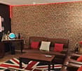 A stylish living room with exposed brick walls, leather sofa, armchair, coffee table, TV, and decorative items on a side table.