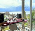 Modern room with large windows offering a scenic mountain and lake view, equipped with a DJ controller, speakers, a chair, and a small table.