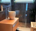 Modern bathroom with a wooden vanity, large sink, glass-enclosed shower, and dark tiled walls.