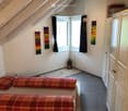 Cozy attic bedroom with slanted wooden ceiling, two red plaid sofas, white wardrobe, wall art, and a small lantern on the floor.